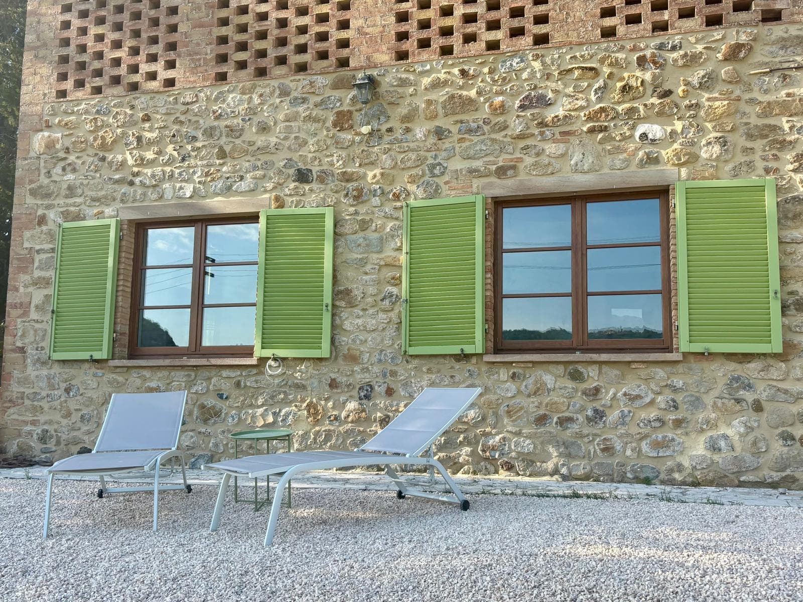 Villa stone facade with green shutters and sun loungers