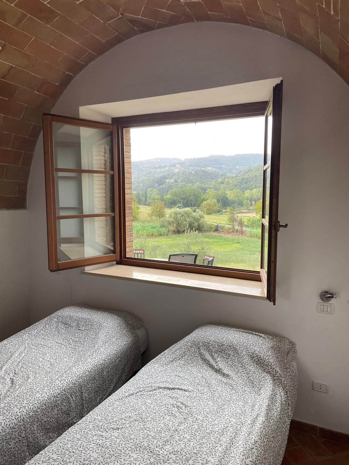 Twin bedroom under a brick arch with a countryside window