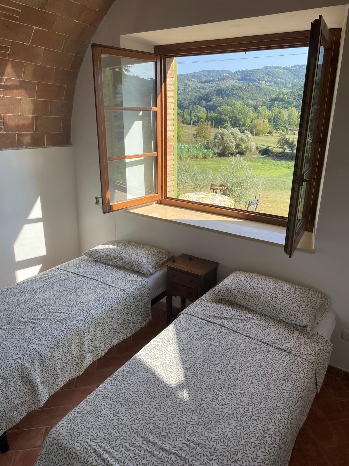 Twin bedroom with a sunlit brick arch and countryside window
